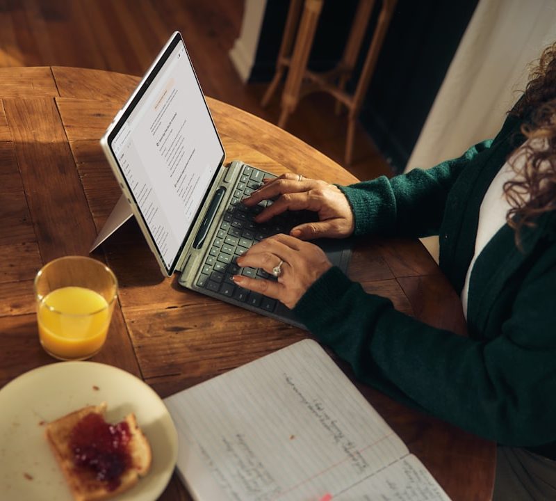 Woman typing on laptop at wooden table with breakfast.